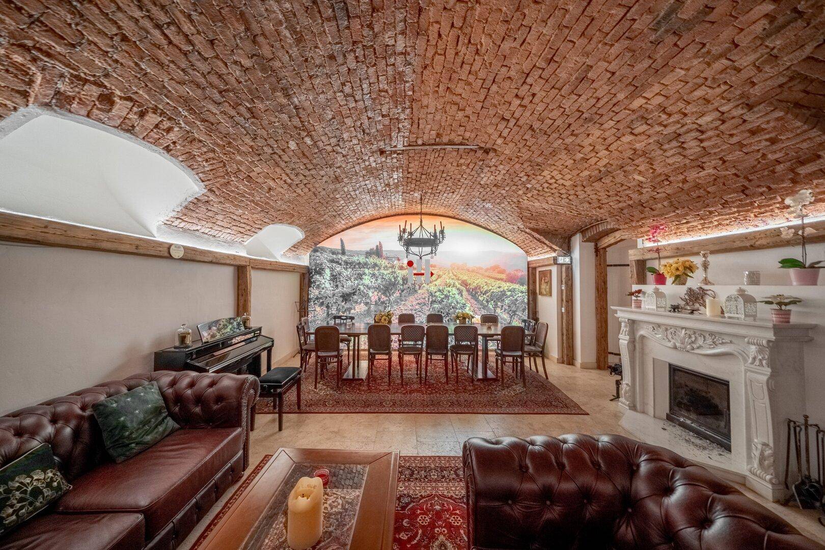 Großer Wohn-Essbereich im Keller mit Ziegelgewölbe, Kamin und Wandbild einer Weinlandschaft.