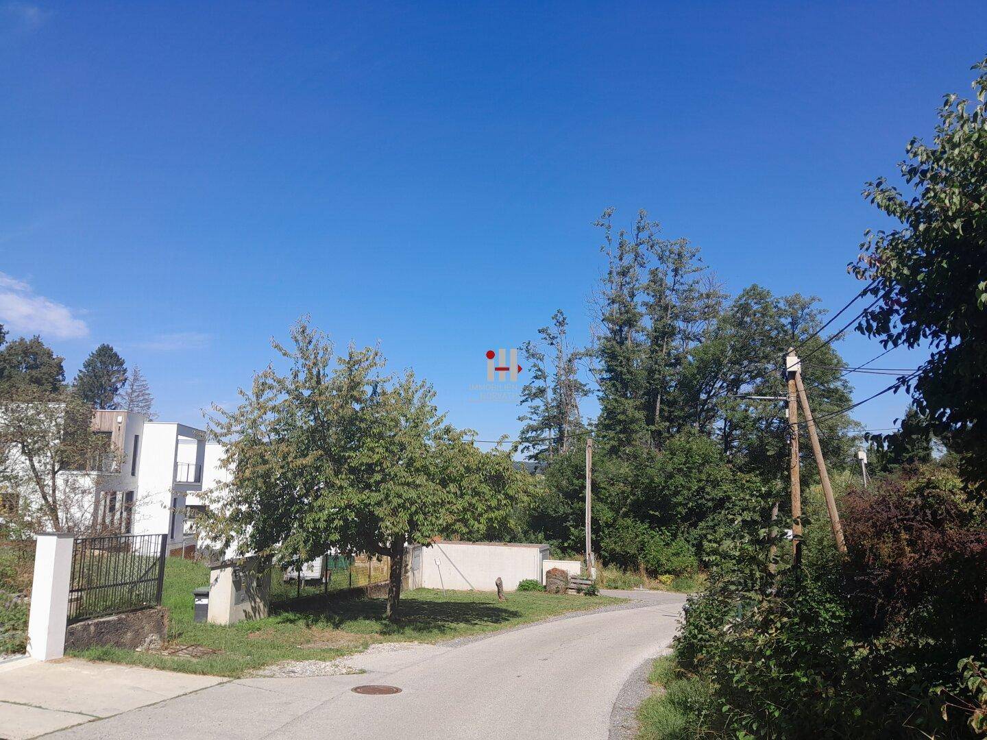 Blick auf eine ruhige Straße mit modernen Häusern und viel Grün unter blauem Himmel.
