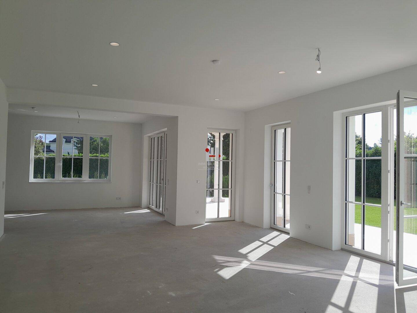 Geräumiger, heller Wohnbereich im Rohbau mit großen Fenstern und Zugang zum Garten.