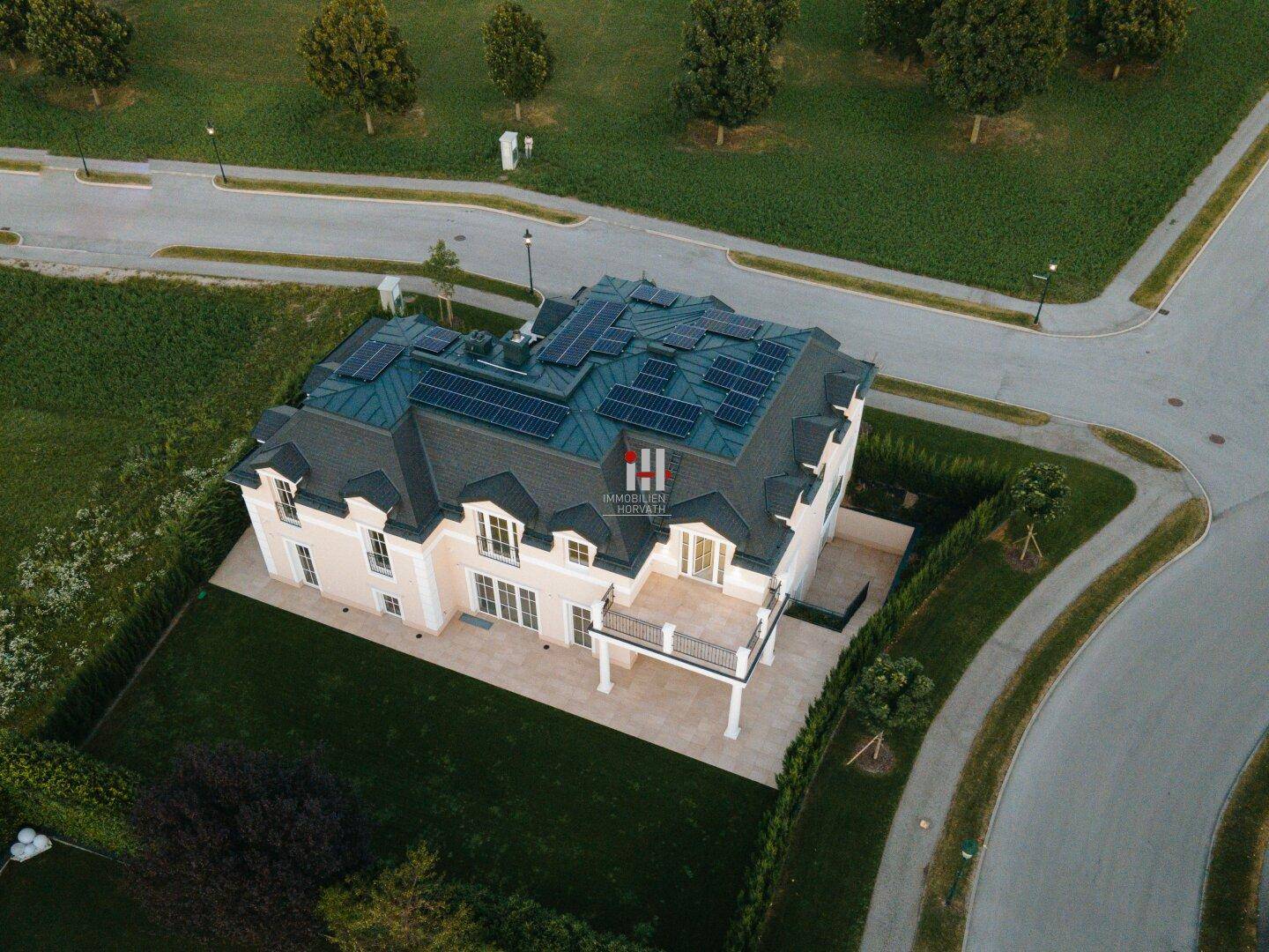 Luftaufnahme eines luxuriösen Hauses mit Solaranlage auf dem Dach und großem Garten.