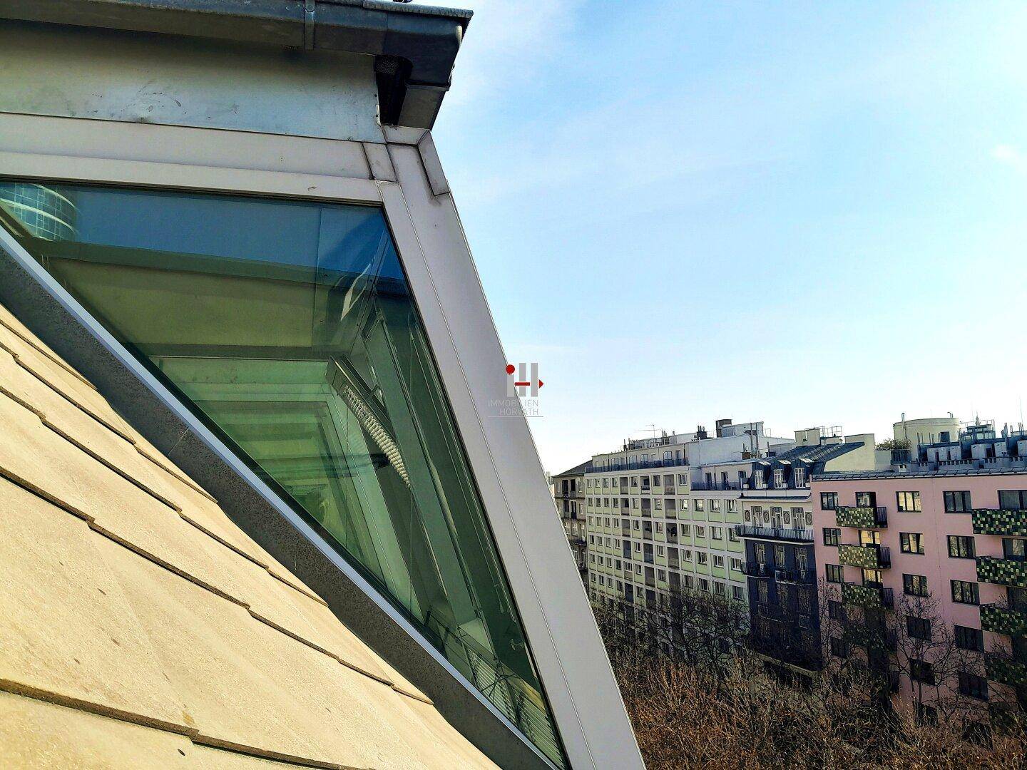 Dachansicht mit schrägen Glasfenstern und Blick auf städtische Gebäude.