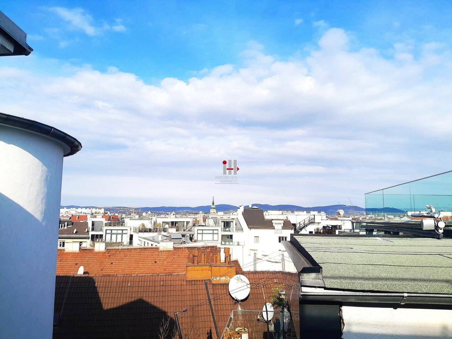 Panoramablick über die Dächer der Stadt mit Bergen am Horizont unter blauem Himmel.