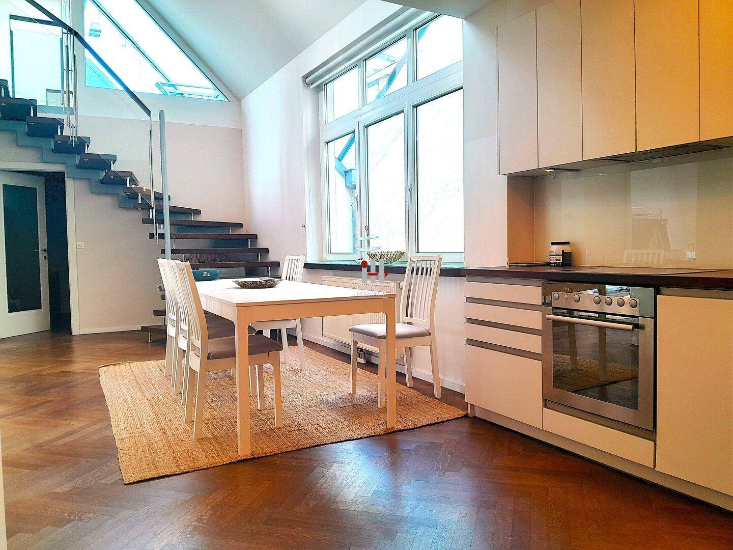 Offene Küche mit Essbereich, modernen Schränken und großen Fenstern mit Blick nach draußen.