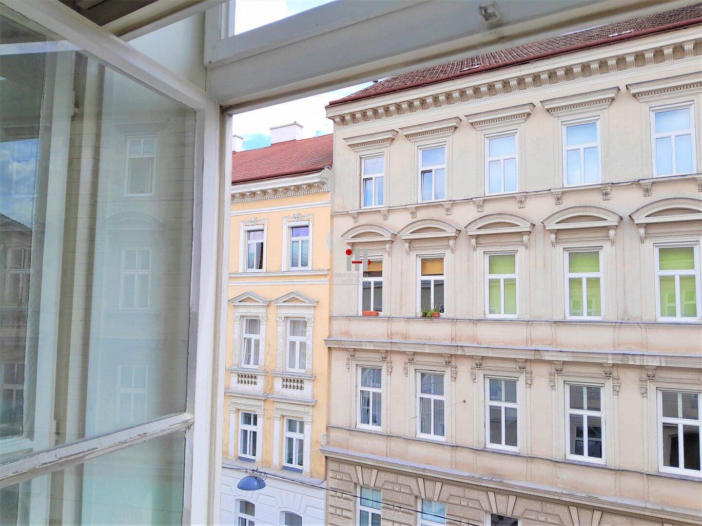 Blick aus dem Fenster auf gegenüberliegende Altbaufassaden mit vielen Fenstern und dekorativen Elementen.