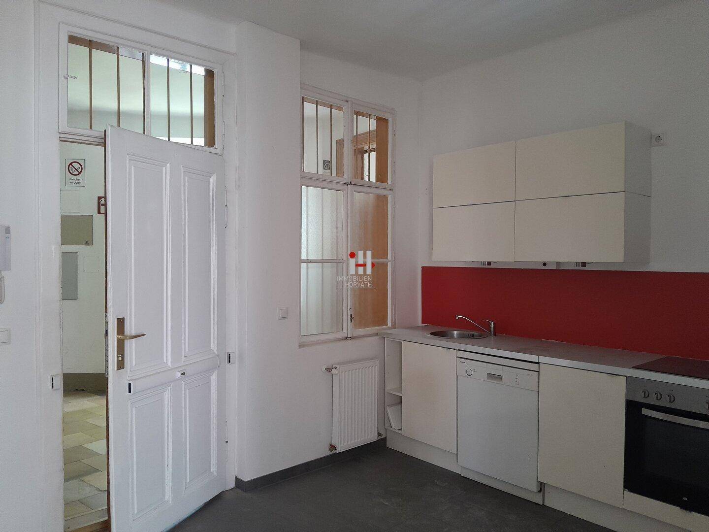Funktionale Küche mit weißen Hängeschränken, roter Rückwand und integrierten Geräten wie Geschirrspüler und Ofen.