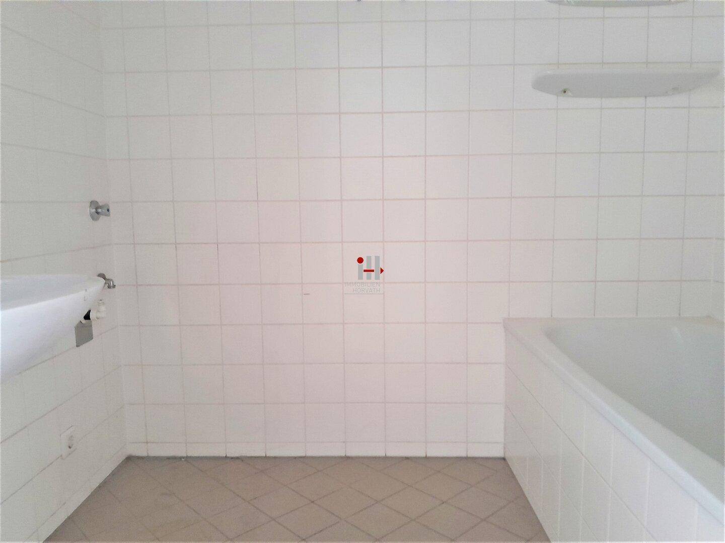Badezimmer mit weißen Wand- und Bodenfliesen, ausgestattet mit einer Badewanne und Waschbeckenanschluss.