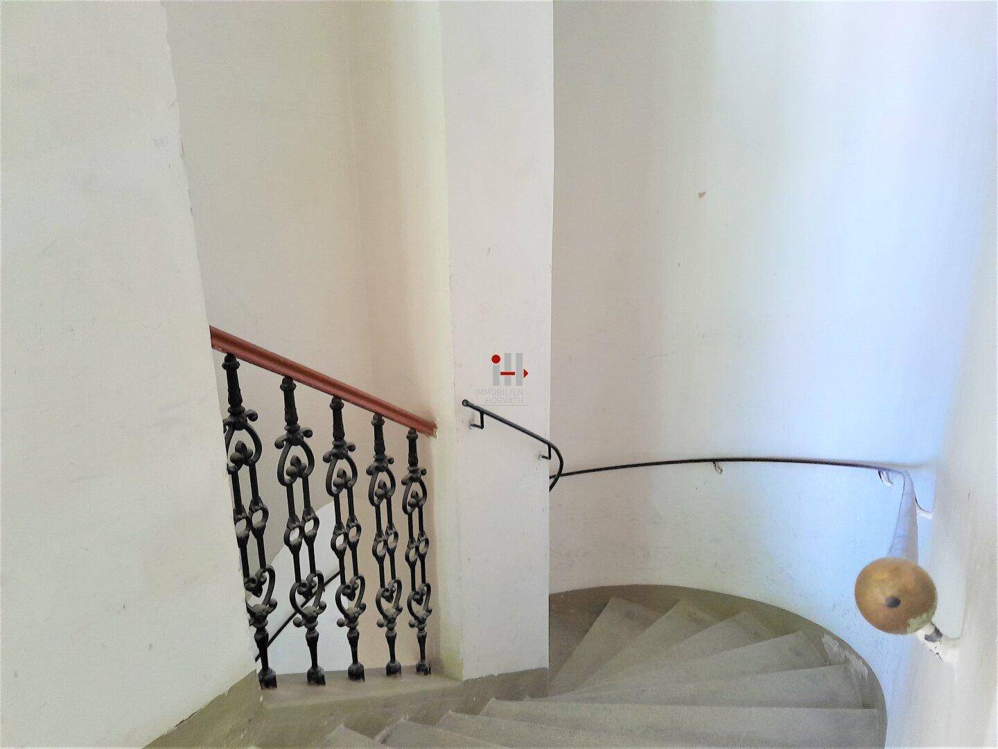 Historisches Treppenhaus mit geschwungenen Stufen, schmiedeeisernem Geländer und Holzhandlauf.