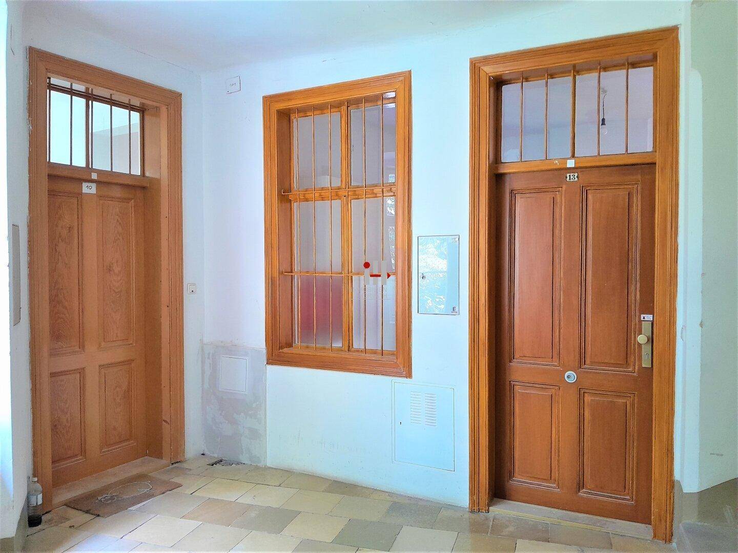 Flur mit zwei traditionellen Holztüren, einem Fenster mit Gitter und Fliesenboden.