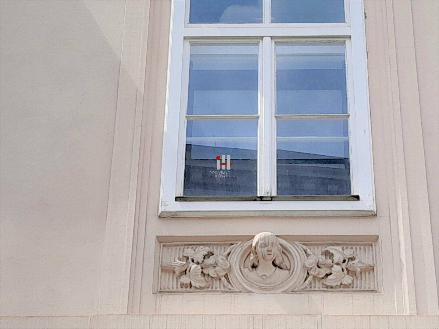 Detailansicht eines Fensters mit weißem Rahmen und kunstvollen Stuckverzierungen an der Fassade.