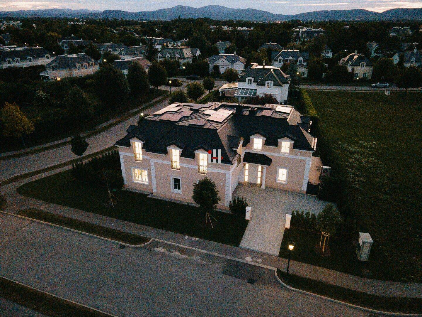 Luftaufnahme eines modernen Hauses mit Solaranlage, gepflegtem Garten und Bergblick in einer ruhigen Wohnsiedlung.