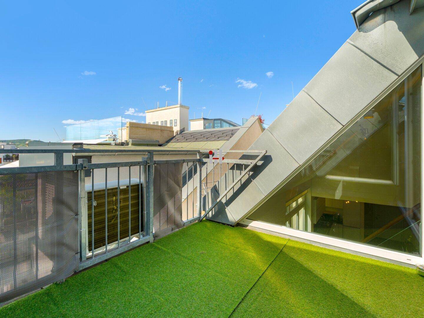 Dachterrasse mit Kunstrasen, Metallgeländer und weitem Blick über die Stadt.