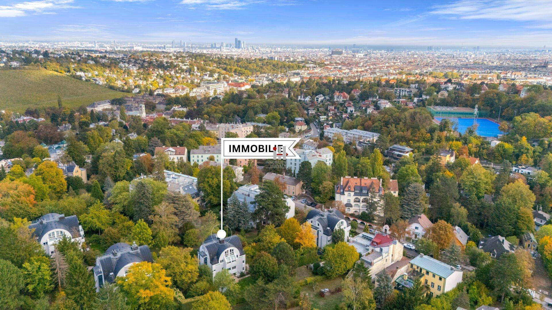 Weitläufige Luftaufnahme einer grünen Wohngegend mit Blick auf die Stadt am Horizont.