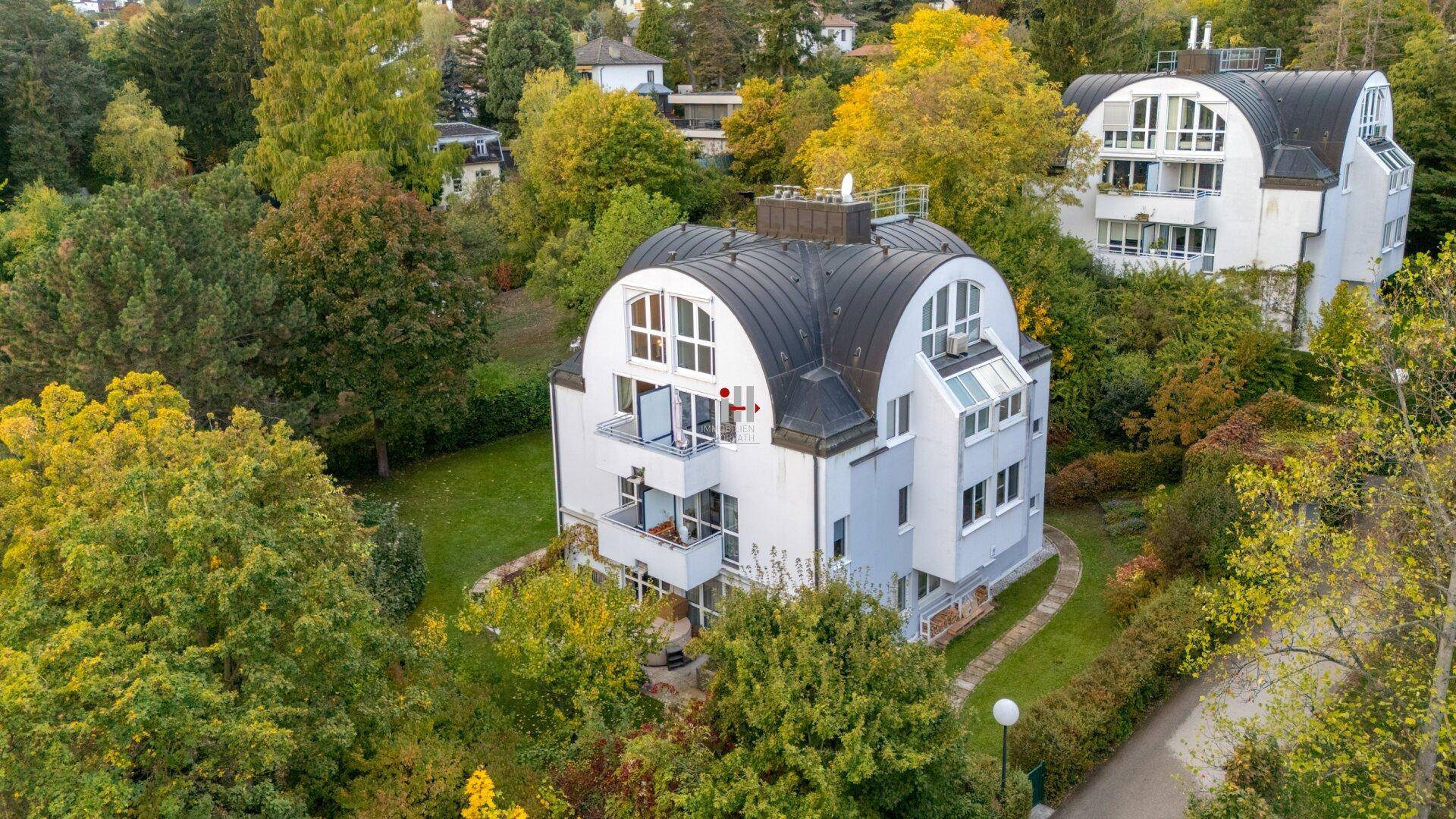 Ansicht eines modernen Wohngebäudes mit markantem Dach und Balkonen, umgeben von Bäumen.