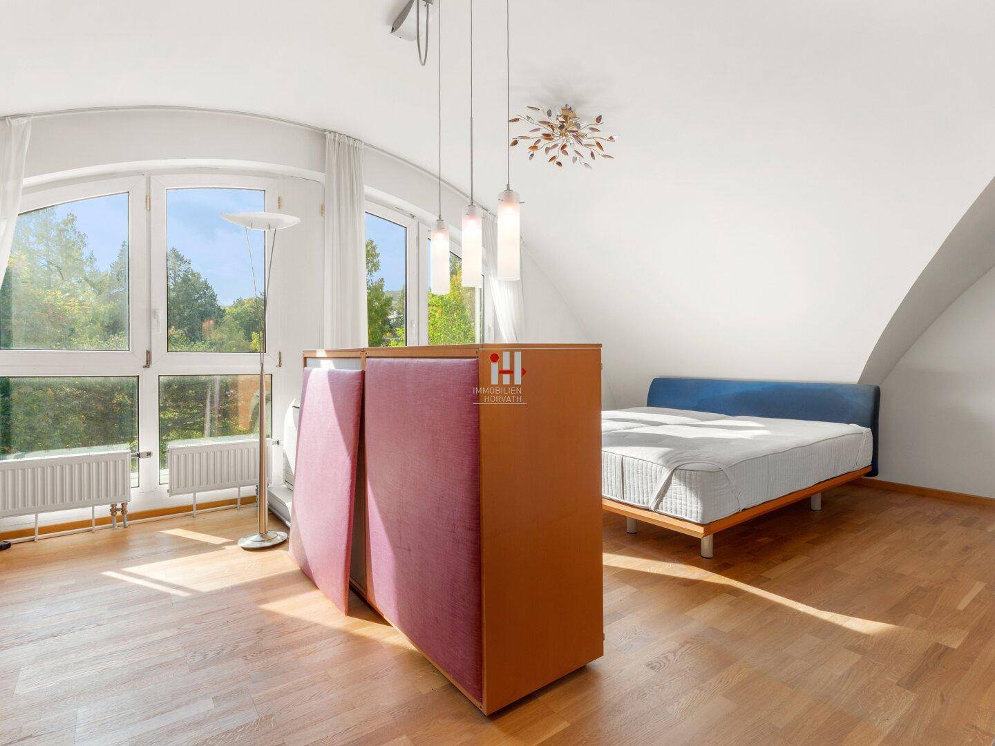 Helles Schlafzimmer mit Holzboden, großen Fenstern und Dachschrägen, offen gestaltet.
