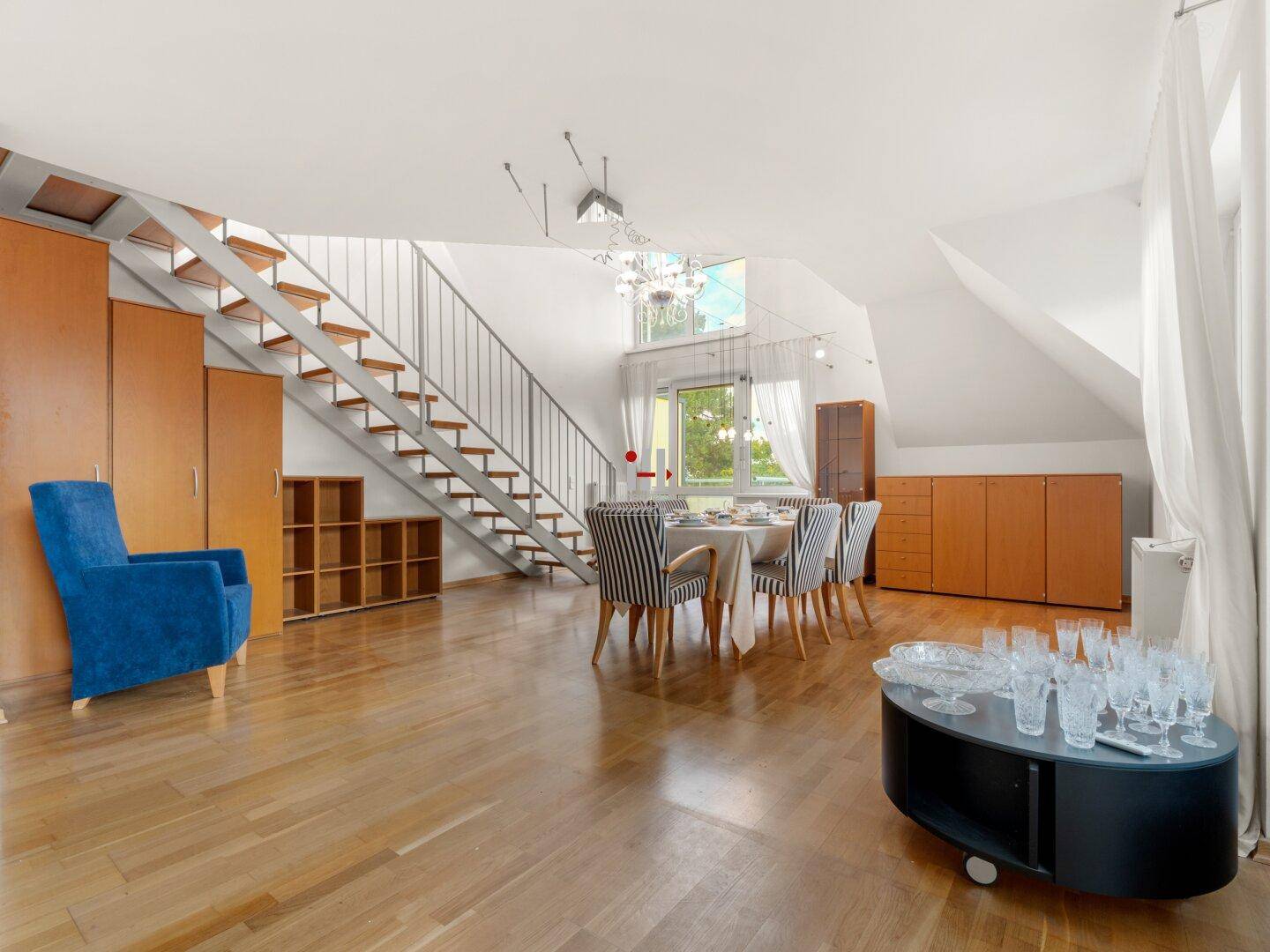 Heller Wohn- und Essbereich mit Holzboden, Dachschrägen und einer offenen Treppe.