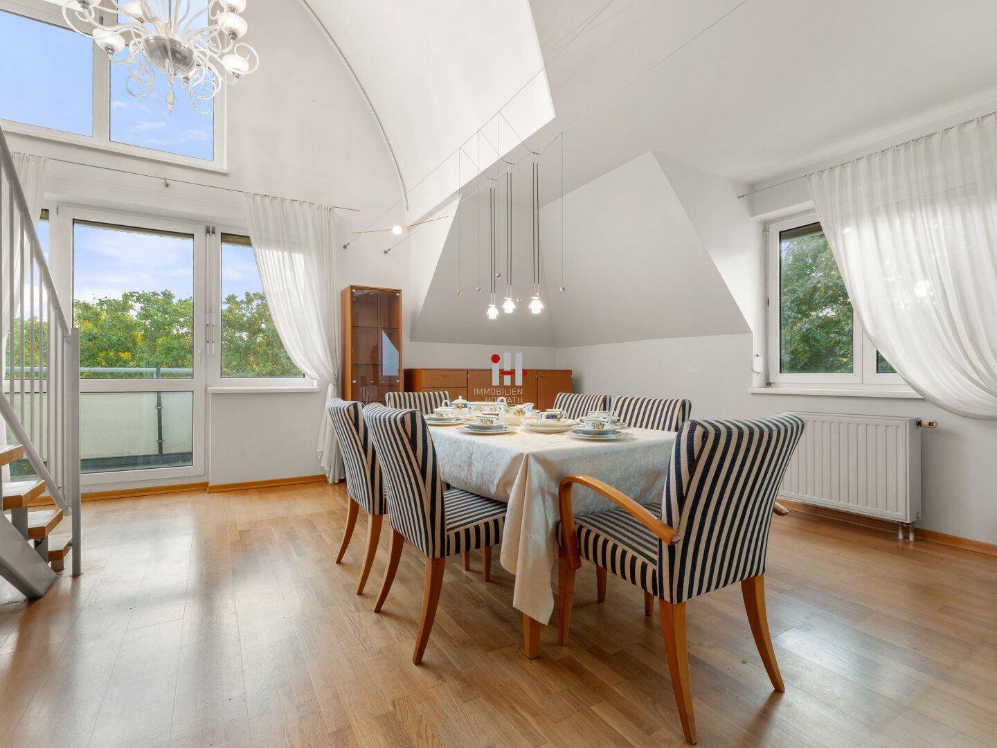 Essbereich mit Holzboden, großen Fenstern und Zugang zu einem Balkon, unter Dachschrägen.