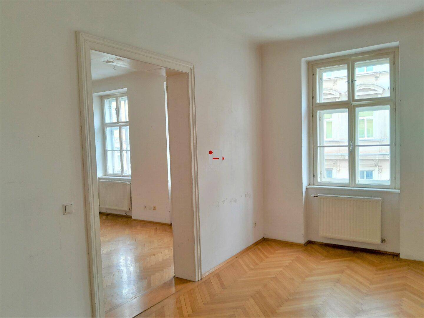 Geräumiges, leeres Zimmer mit Parkettboden und zwei Fenstern, die viel Tageslicht hereinlassen.