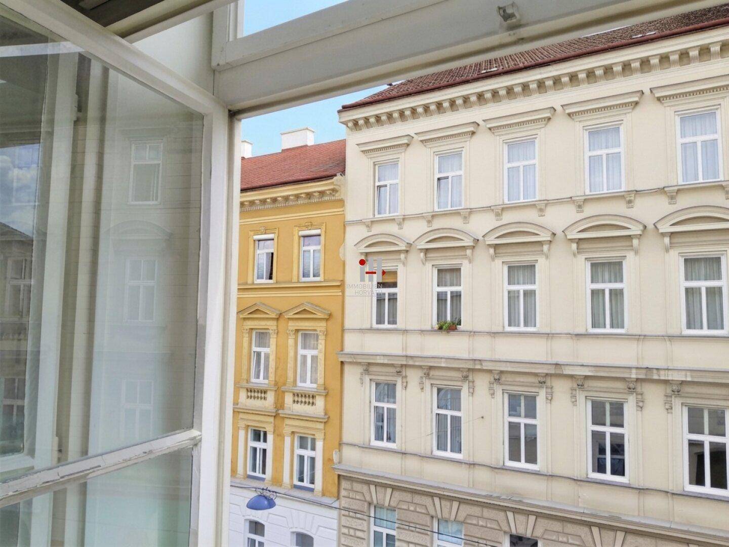 Blick aus einem Fenster auf die gegenüberliegenden historischen Gebäude mit gelben und beigen Fassaden.