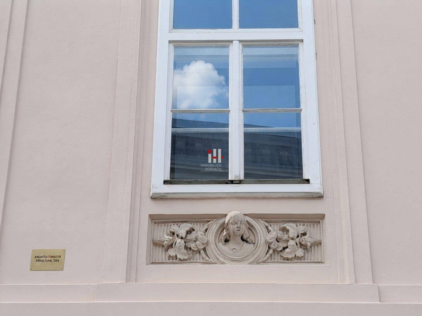 Detail der historischen Fassade mit einem Fenster und kunstvollen Stuckverzierungen unterhalb der Fensterbank.