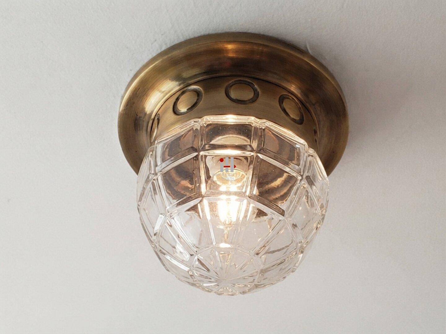 Detailaufnahme einer klassischen Deckenleuchte aus Messing mit facettiertem Glas in einem Innenraum.