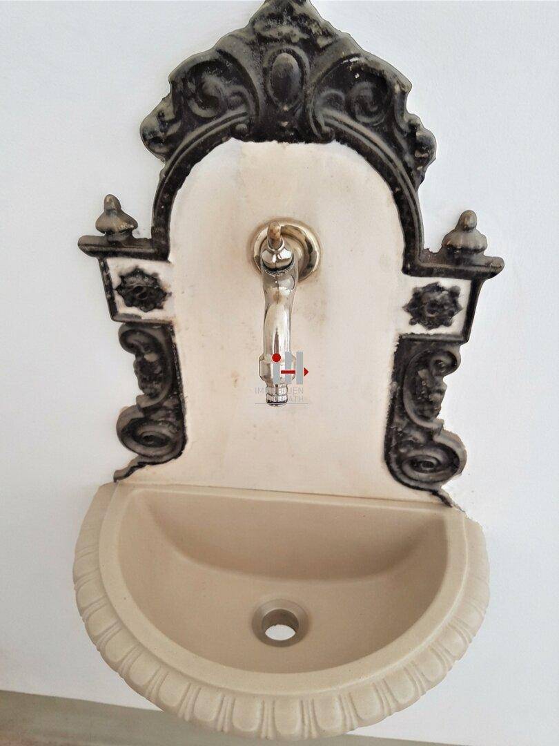 Dekorativer Wandbrunnen im Vintage-Stil mit schmiedeeisernen Elementen und einem kleinen Becken.