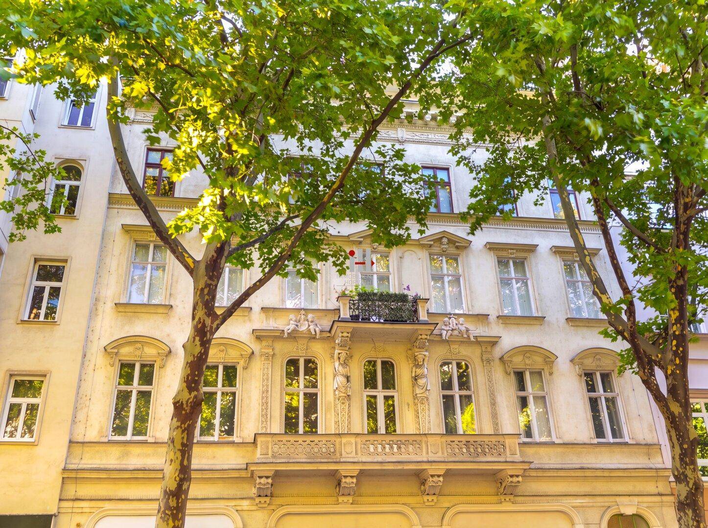 Historische Fassade eines Altbaus mit reich verzierten Balkonen und großen Fenstern.