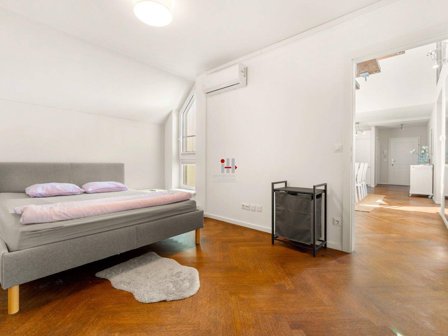 Helles Schlafzimmer mit Parkettboden, Dachschräge und Blick in den offenen Wohnbereich.