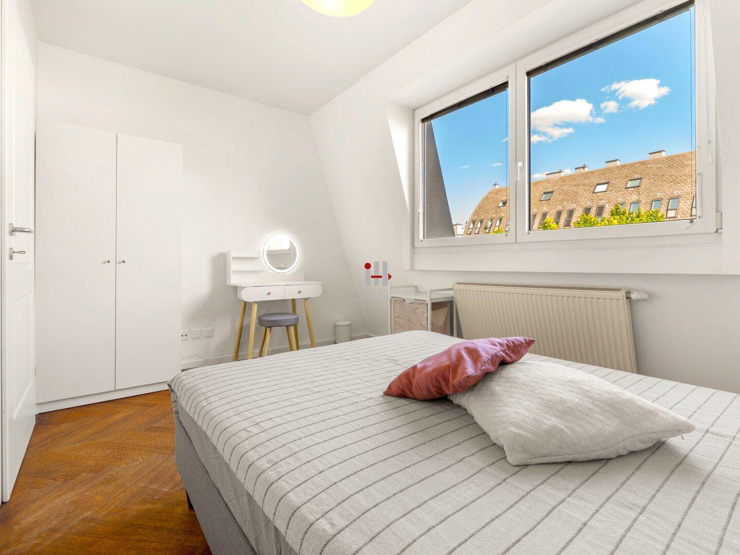 Helles Schlafzimmer mit Parkettboden, weißem Kleiderschrank und Schminktisch am Fenster.