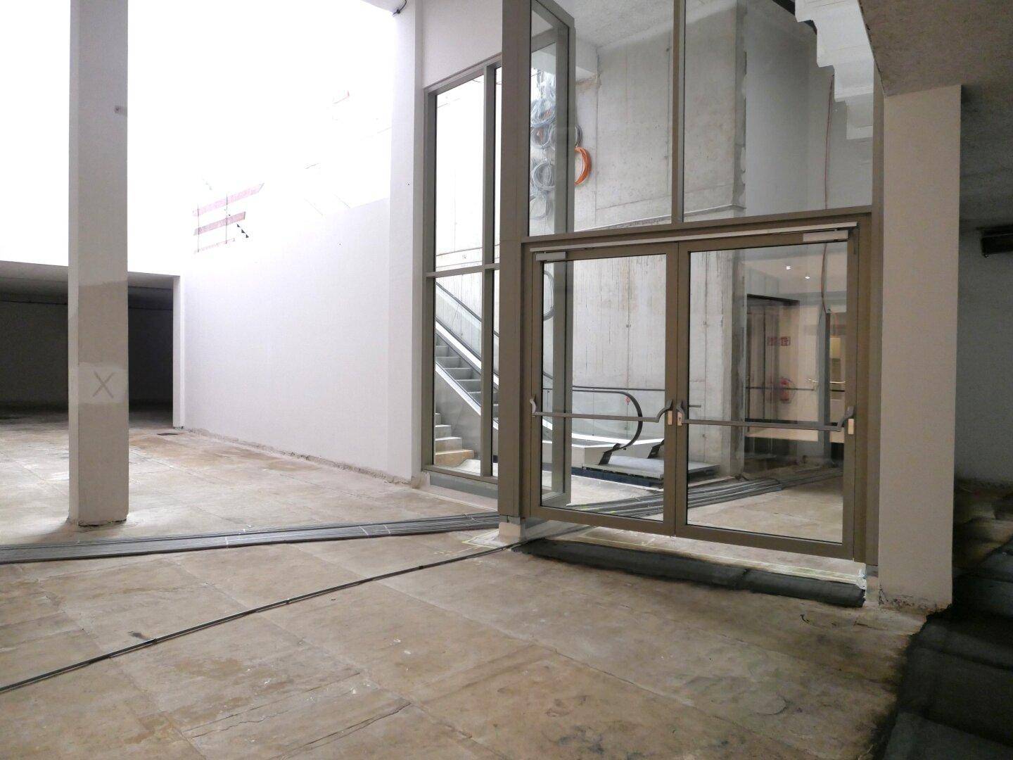 Leerer Gewerberaum im Rohbau mit sichtbarem Aufzug und Rolltreppe, bereit für den Innenausbau.