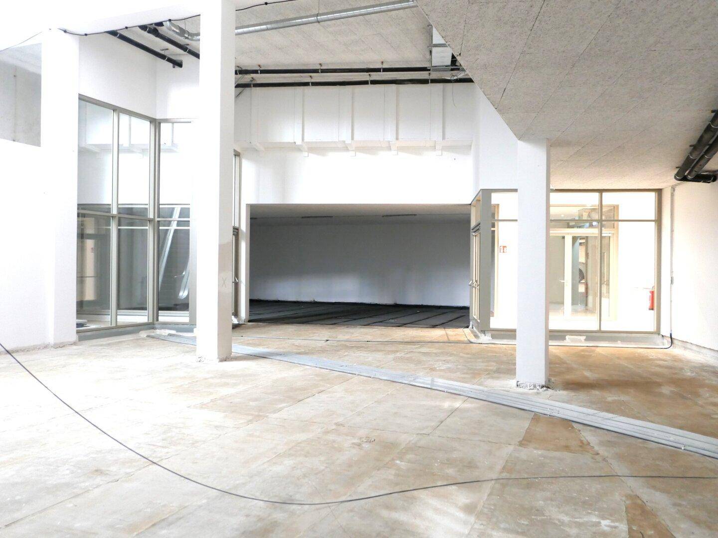Großer, leerer Gewerberaum im Rohbau mit hohen Decken und sichtbaren Installationen, bereit für den Ausbau.