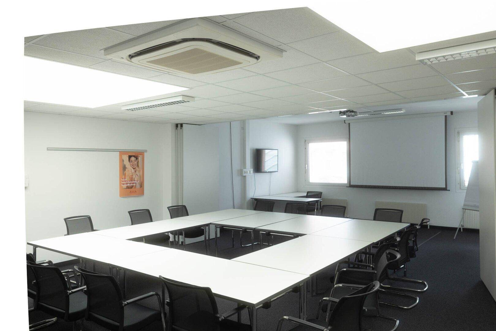 Geräumiger Konferenzraum mit U-förmigem Tisch, Projektionsleinwand und Klimaanlage.