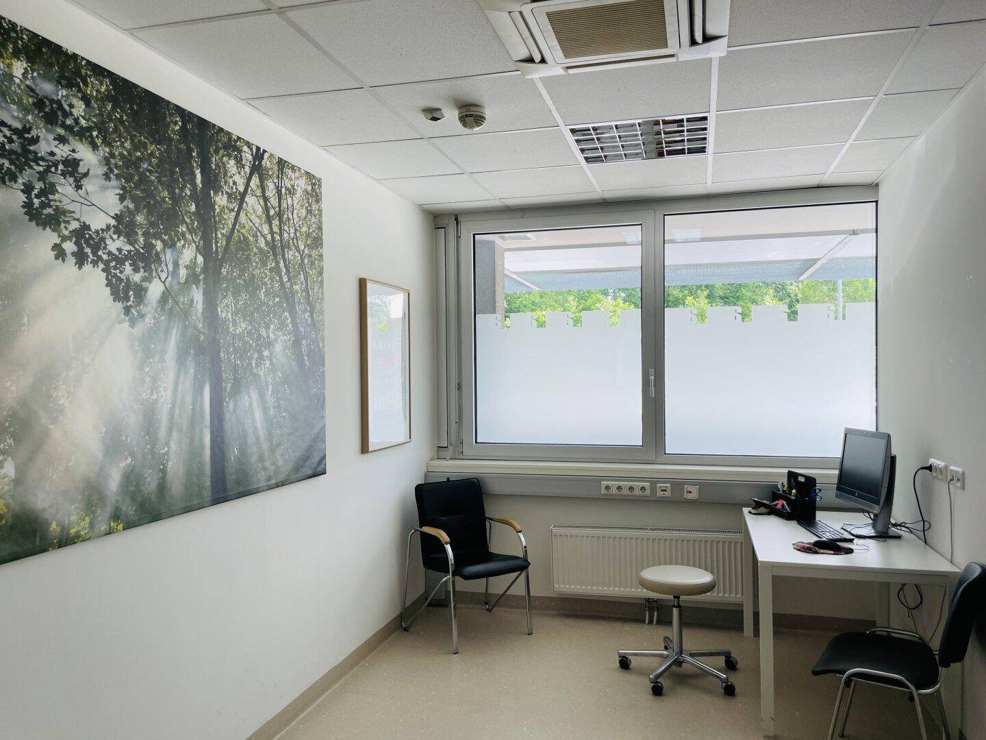 Helles Bürozimmer mit Schreibtisch, Computerarbeitsplatz und großem Fenster mit Sichtschutzfolie und Klimaanlage.