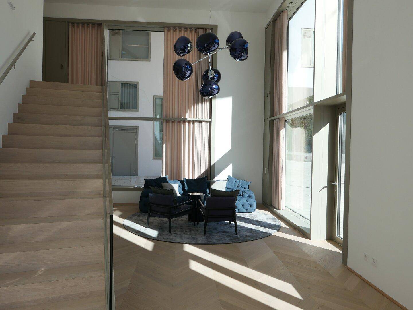 Eingangsbereich mit Holztreppe und einem stilvollen Loungebereich, beleuchtet durch große Fenster.
