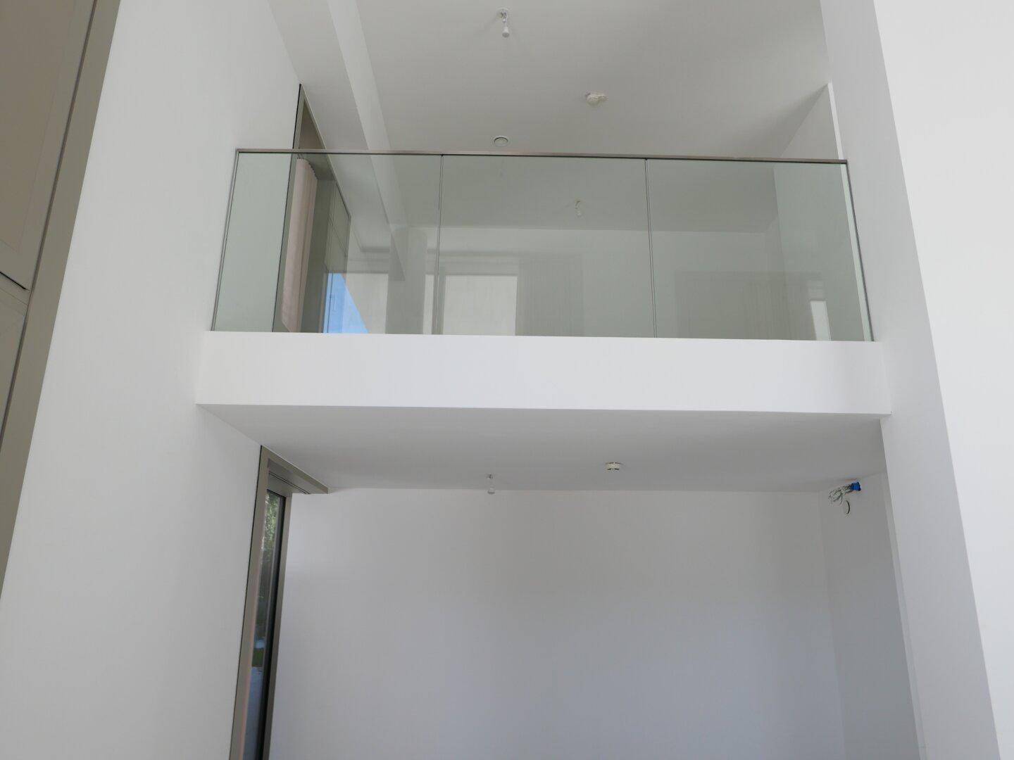 Obere Galerie mit modernem Glasgeländer und Blick auf den darunterliegenden offenen Bereich.