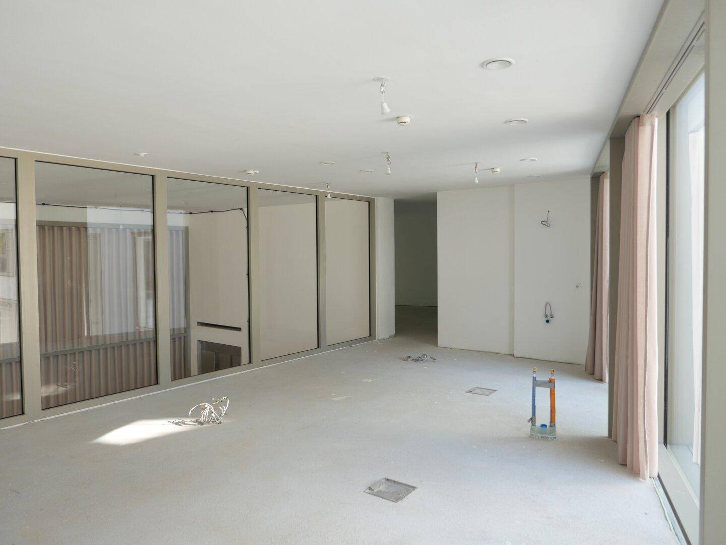 Geräumiger, heller Innenraum mit großen Fensterfronten und einem modernen, minimalistischen Design im Rohbauzustand.