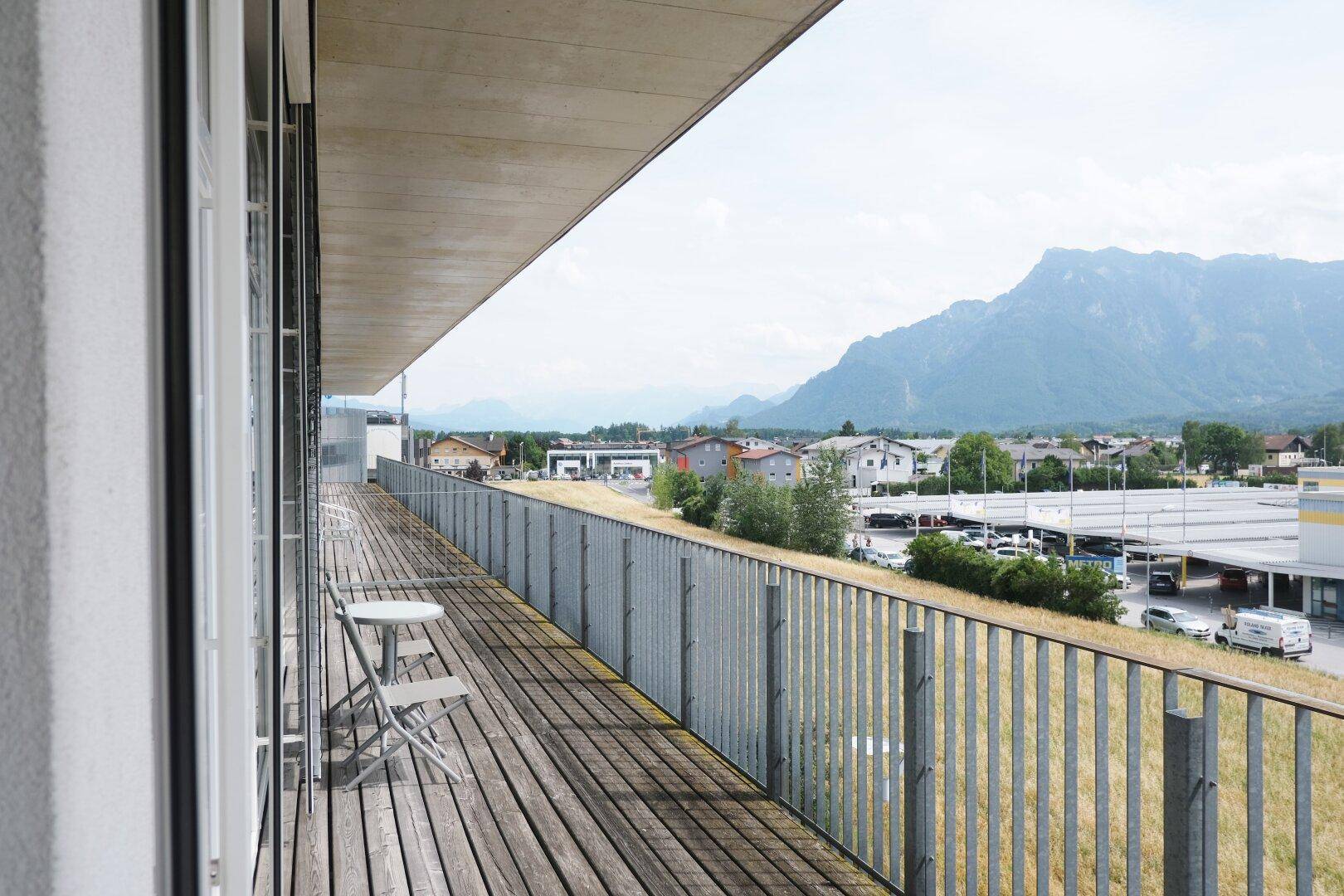Langer Balkon mit Holzboden, Metallgeländer und weitem Blick auf die Berge und die Umgebung.