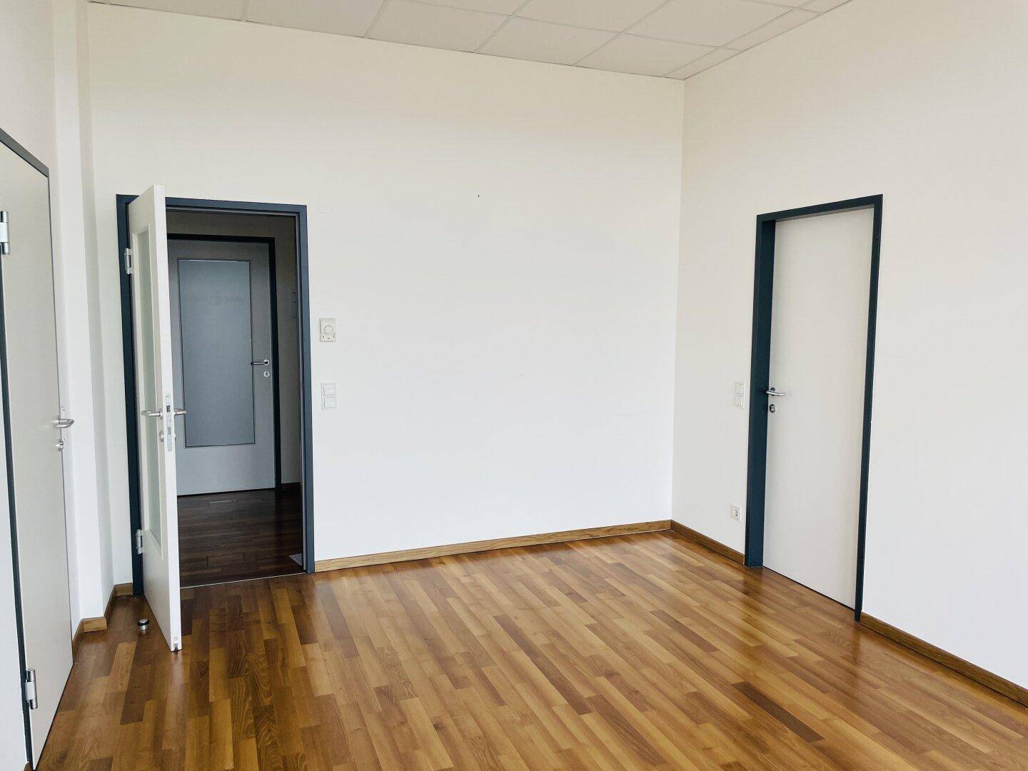 Leerer Büroraum mit Holzboden und mehreren Türen, die zu anderen Bereichen führen.