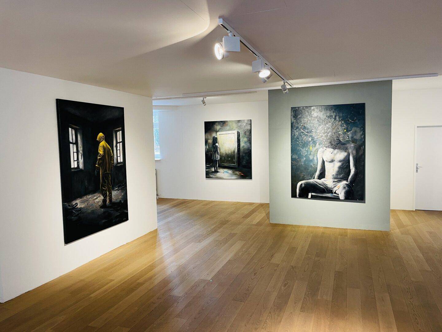 Weitläufiger, heller Raum mit Holzboden, weißen Wänden und zeitgenössischen Kunstwerken unter Deckenspots.