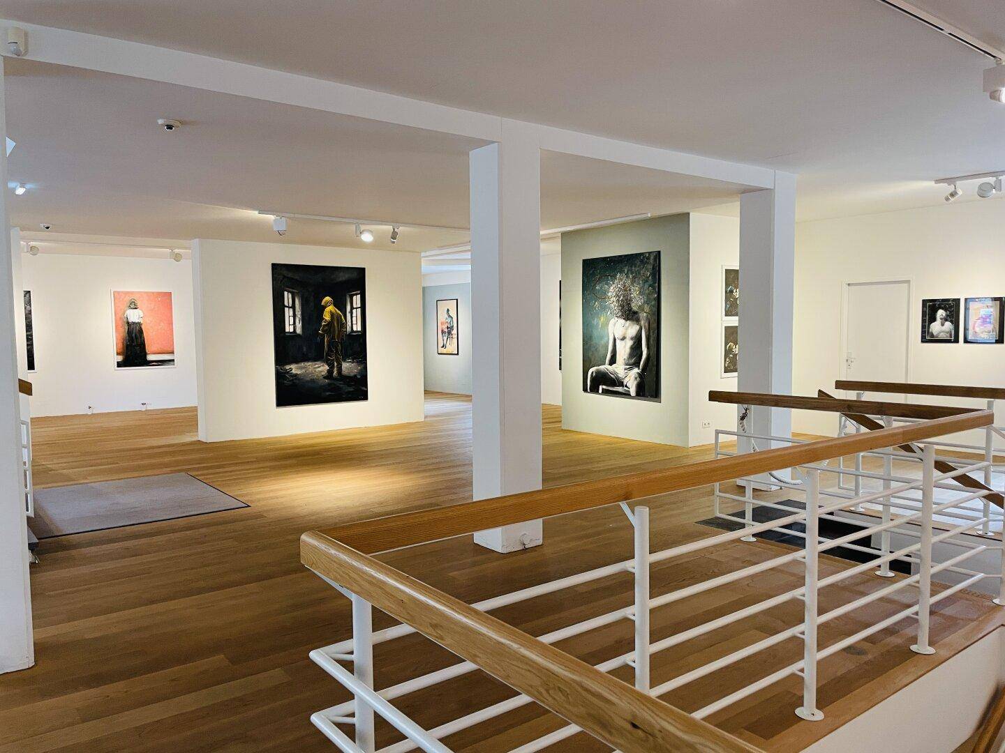 Weitläufiger, heller Raum mit Holzboden, weißen Wänden und Kunstwerken, verbunden durch eine offene Treppe.