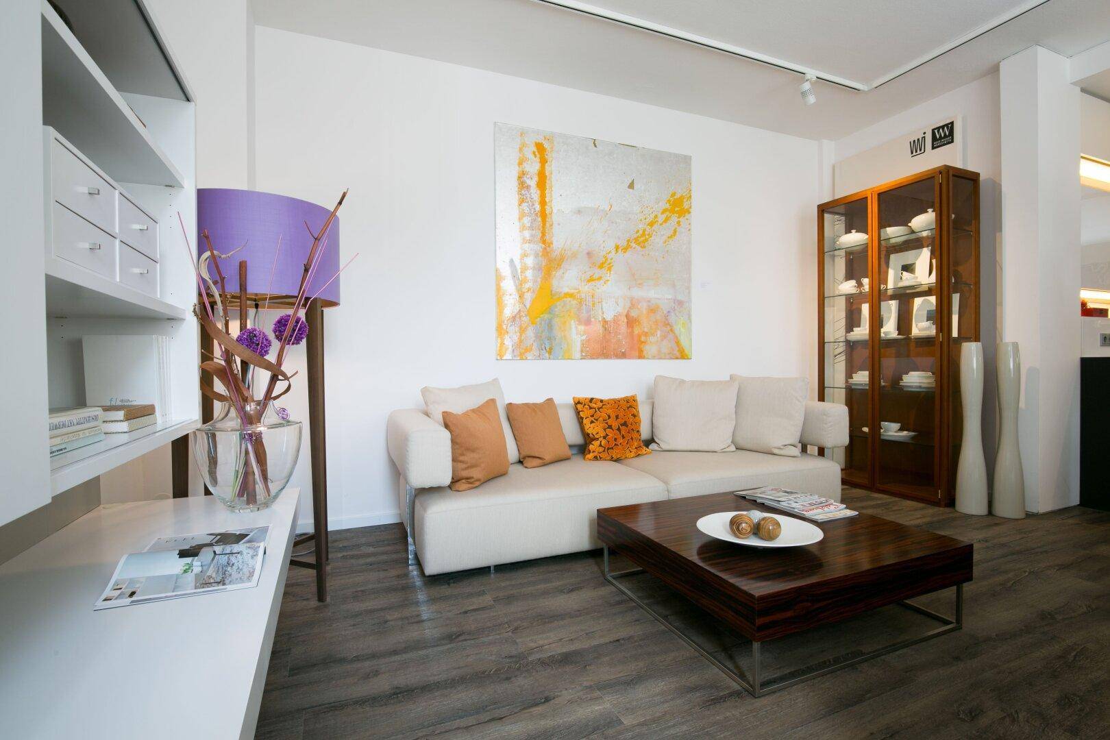Gemütliches Wohnzimmer mit weißem Sofa, Holztisch und farbenfroher Kunst, einladend eingerichtet.