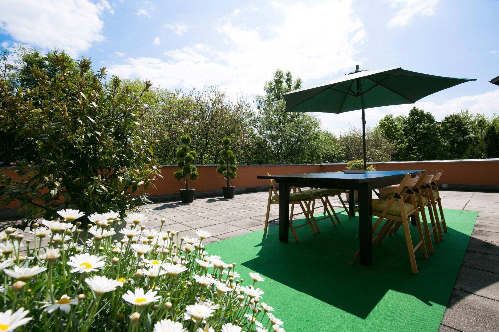 Geräumige Dachterrasse mit Esstisch, Sonnenschirm und vielen Pflanzen, perfekt für Mahlzeiten im Freien.