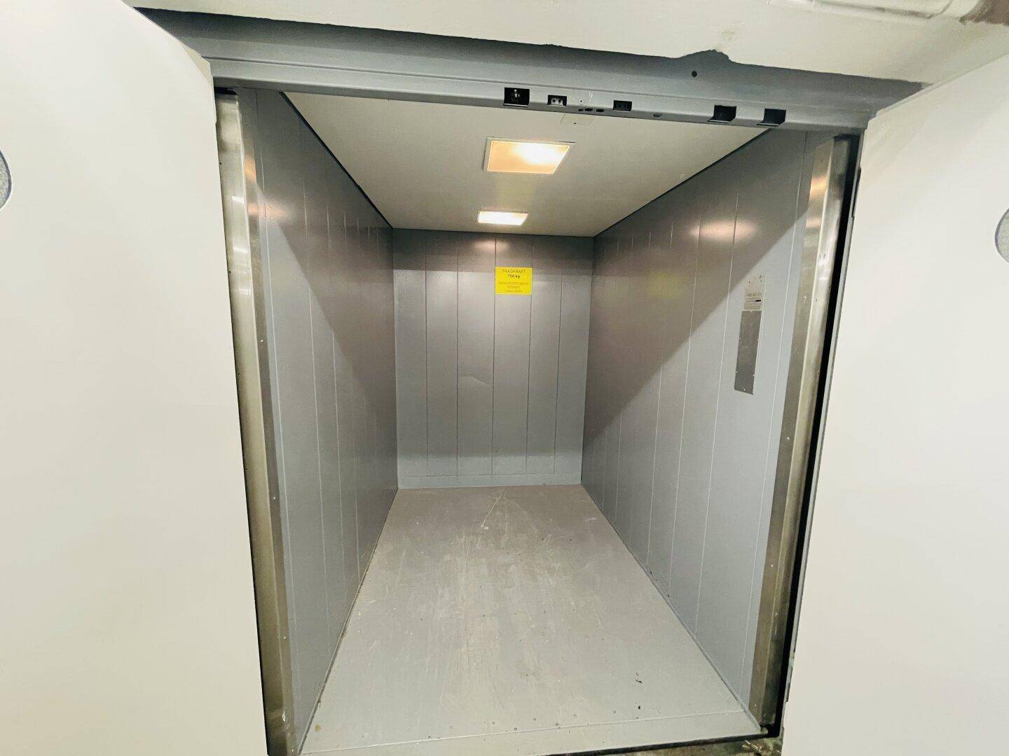 Innenansicht eines geräumigen Lastenaufzugs mit Metallwänden und Deckenbeleuchtung.