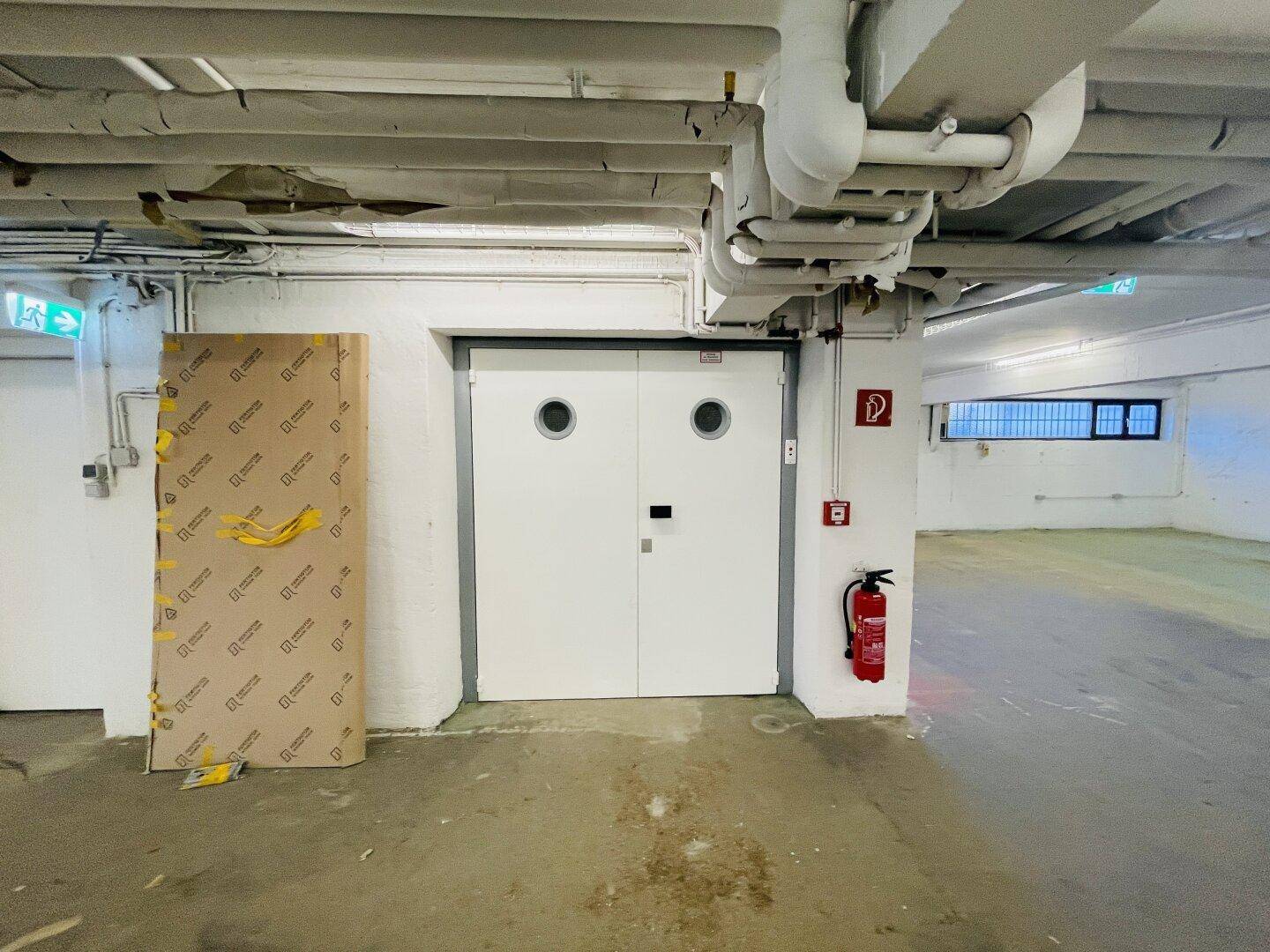 Industriebereich im Untergeschoss mit großer Doppeltür, sichtbaren Leitungen und Brandschutzvorrichtungen.
