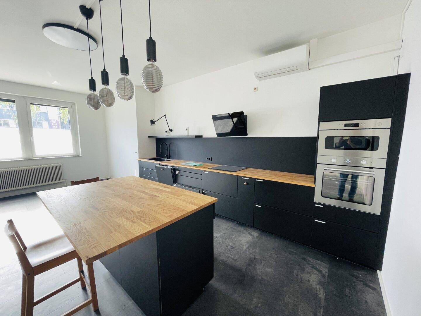 Moderne schwarze Küche mit Holzarbeitsplatte, Kochinsel und integrierten Geräten.