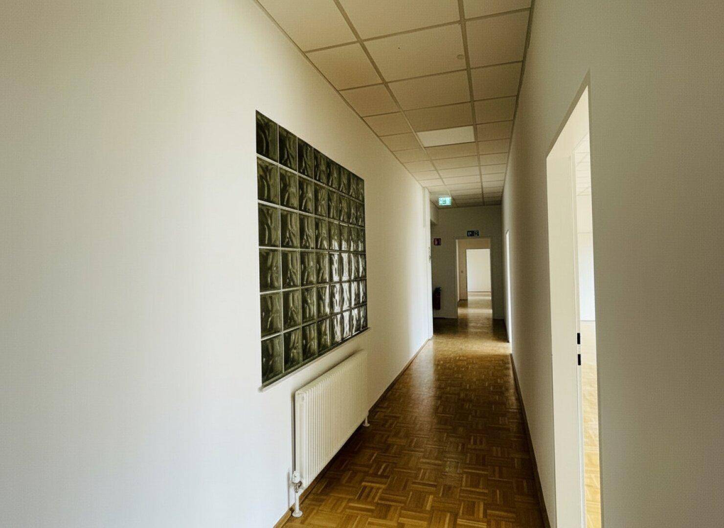 Langer Flur mit Fischgrätparkett, Glasbausteinwand und Rasterdecke.