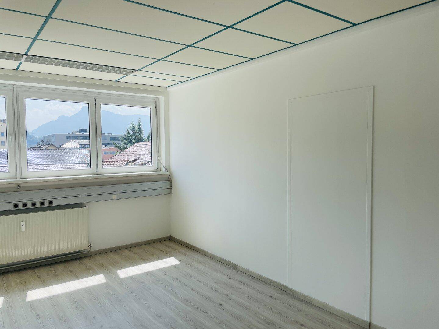 Heller Büroraum mit Laminatboden und Blick auf die umliegende Berglandschaft.