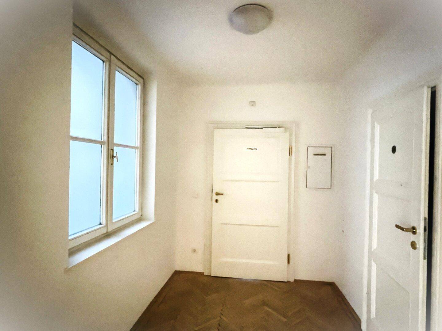 Kleiner Eingangsbereich mit Fenster, weißer Tür und Fischgrätparkett, hell und funktional.