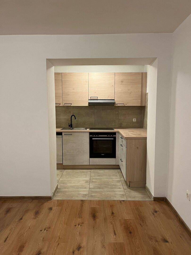 Offene Küchenzeile mit hellen Holzschränken und Fliesenboden, vom Wohnbereich aus sichtbar.