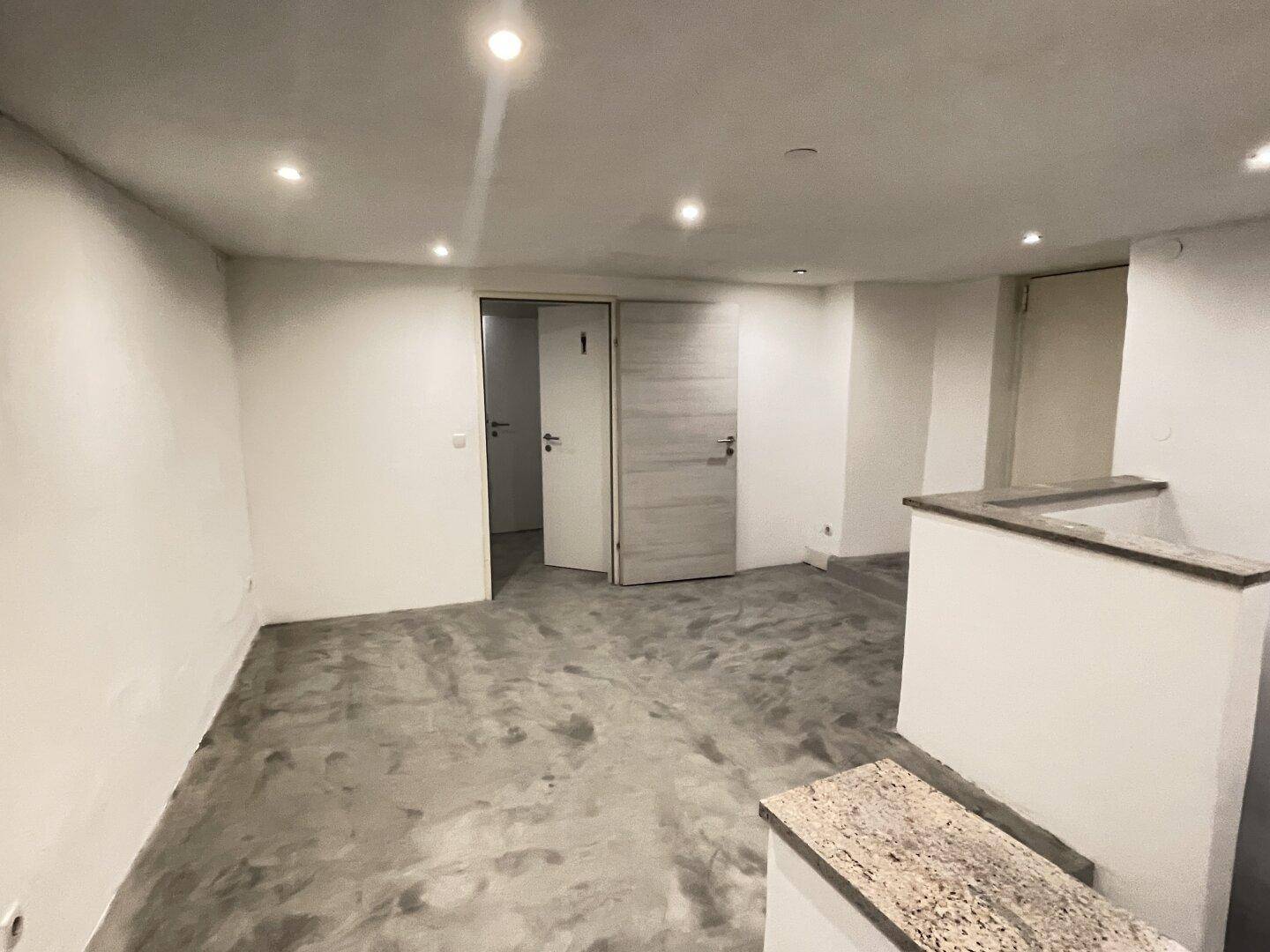 Geräumiger Kellerraum mit Betonboden, Einbaustrahlern und Zugang zu weiteren Räumen.