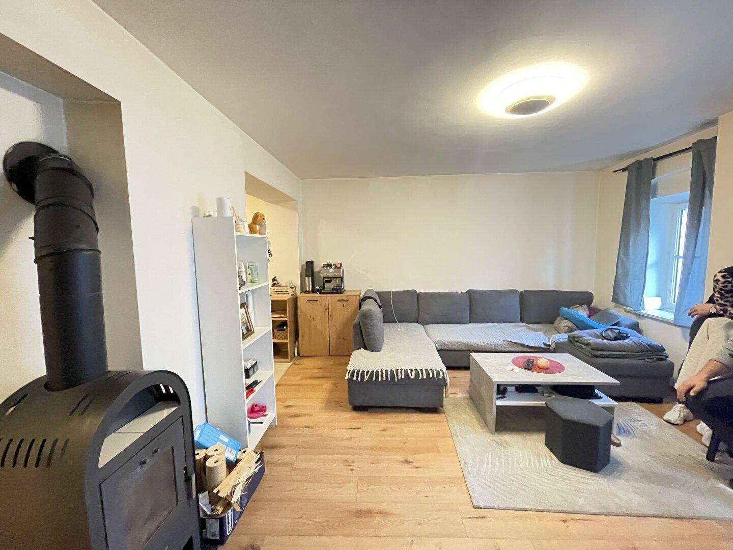 Geräumiges Wohnzimmer mit großem Ecksofa, Holzboden und Kaminofen als zentrales Element.